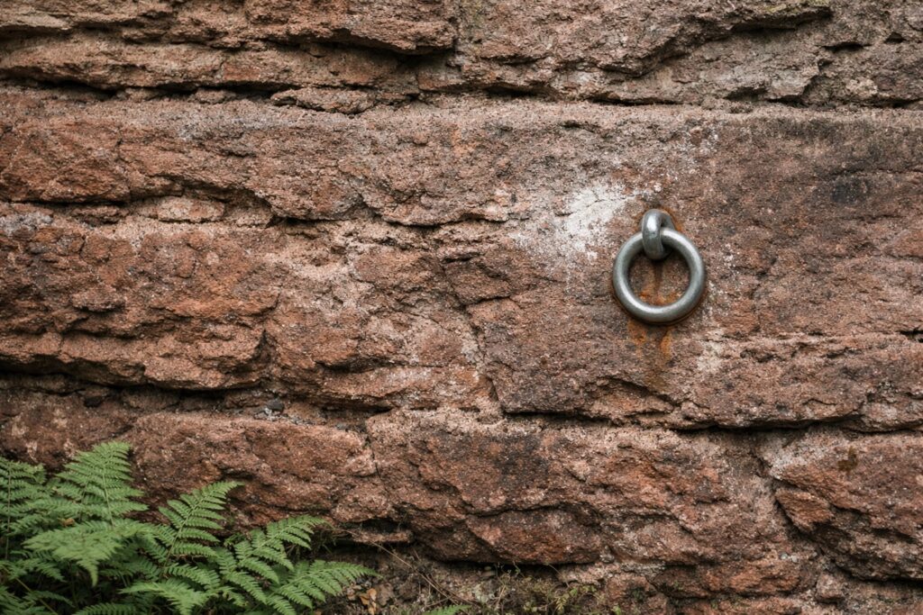 Nahaufnahme eines Metallrings im roten Sandstein, rostige Spuren und Kreideflecken
